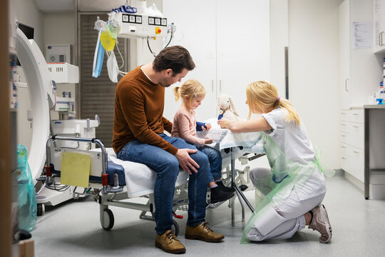 Female doctor holding stuffed toy while playing with girl in ward at hospital