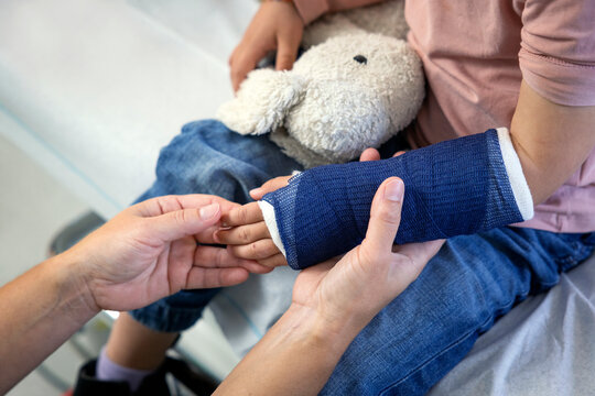 Cropped hand of female pediatrician touching fractured hand of girl in hospital