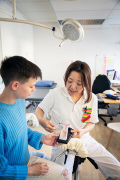 Female doctor explaining IUD insertion in cervix model to teenage boy in clinic