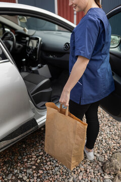 Low section of female healthcare worker with paper bag standing by car