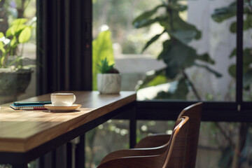 White coffee cup with mobile and note book on wooden counter with seat in cafe and outdoor garden...