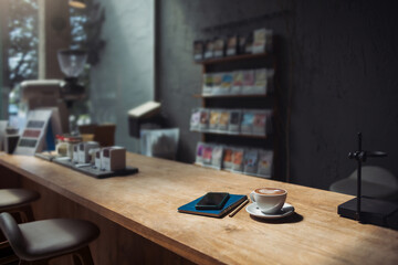 Latte coffee in tea cup with note book and phone on wooden counter in cafe for brakefast