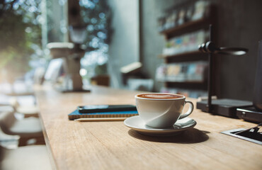 Latte coffee in tea cup with note book and phone on wooden counter in cafe for brakefast, Close-up shot