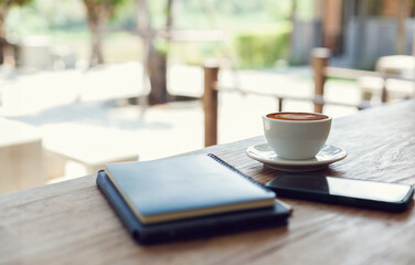 Latte coffee with mobile and note book on wooden table in outdoor cafe