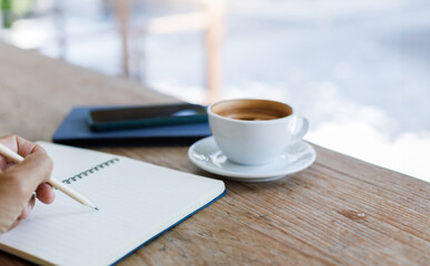 Select focus on hand using pencil taking note in book with coffee cup and mobile on old wooden table