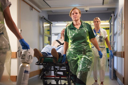 Female paramedics and nurses pushing male patient on gurney for emergency treatment
