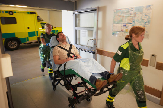 Female rescue workers pulling male patient on gurney for emergency treatment in hospital