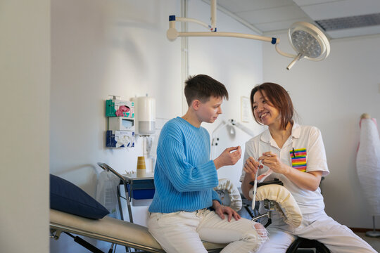 Smiling female gynecologist explaining IUD insertion to gay boy in clinic