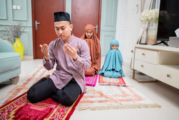 Happy asian muslim family praying jamaah together at home with rug.