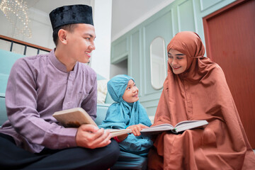 Happy asian muslim family reading koran together at home with rug.