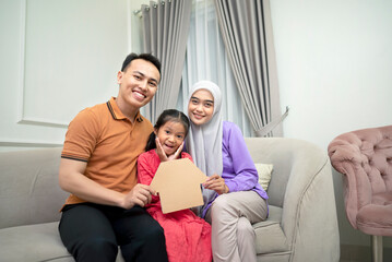 Portrait of Muslim family holding paper house on the couch