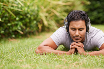 Naklejka na ściany i meble Man, outdoor and headphones on grass, peace and meditating outside for wellness in nature. Male person, backyard and tech to relax, listen and vacation at home or house for peace in music or podcast