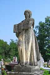 Statue of a woman with a holy writing on a grave in an old cemetery.