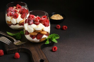 Italian dessert tiramisu with raspberries in a glass on a dark concrete background