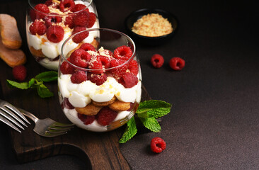 Italian dessert tiramisu with raspberries in a glass on a dark concrete background