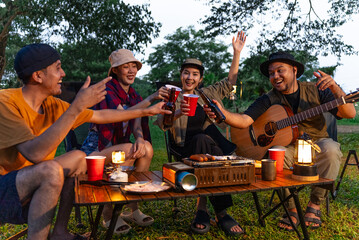 Happy asian diverse group friends enjoy drinking a beer together. They feeling relaxed and refreshing while camping in the nature at night. Recreation and journey outdoor activity lifestyle.