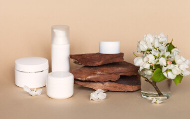 White jars of skin care natural floral cosmetic products on stone podium or pedestal and apple flowers. Cosmetics with apple extract. Spring facial skin care. Front view, close-up, copy space, mock up