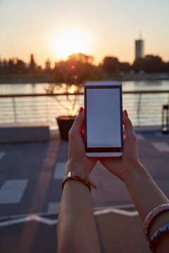 Woman holding cellphone outdoors in sunset time.