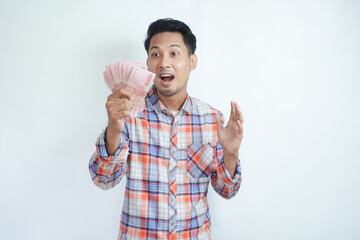 Adult Asian man holding paper money and showing excited face expression when looking at it