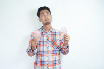 Adult Asian man thinking about something when counting his paper money - obrazy, fototapety, plakaty