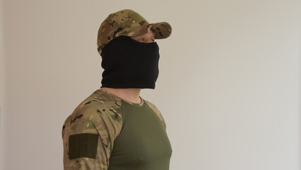 Portrait of a man in military uniform and wearing a black balaclava who looks away hiding his face,...