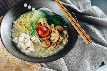 A bowl of soup with noodles, mushrooms, and tomatoes