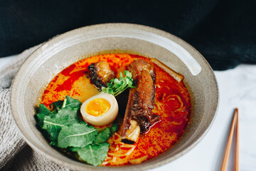 A bowl of soup with a piece of meat and a green leaf