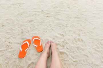 Barefoot toes in sand beside a pair of vibrant orange sandals fashion on a sandy beach texture evoking a relaxed summer day vibe and lifestyle freedom travel on vacation