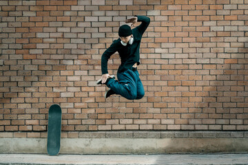 Full length of Asian male fashionable stylish jumping in front of a brick wall