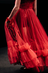 Details of a lush red organza evening dress on a female figure on a black background. Feminine...