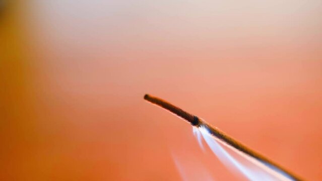 The tip of a smoking incense stick close-up on a blurred background