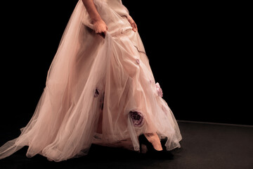 Details of long evening beige chic lush dress on a female figure on a black background. Feminine...