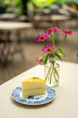 A slice of Lemon Cake, delicately decorated with sprigs of thyme, showcases its layers of airy chiffon and tangy lemon sauce. 