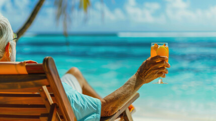 Happy retired elderly man sitting on a lounge chair, drinking cocktail on the beach enjoying his vacation
