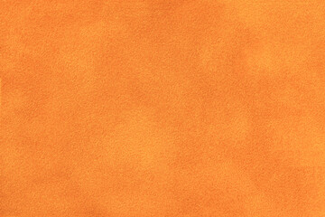 Bright orange matte background of suede fabric, closeup. Velvet texture of pumpkin textile, macro.