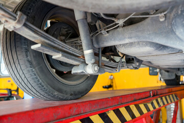 A car is on a lift showing its underside with a wheel, leaf spring  and suspension components...