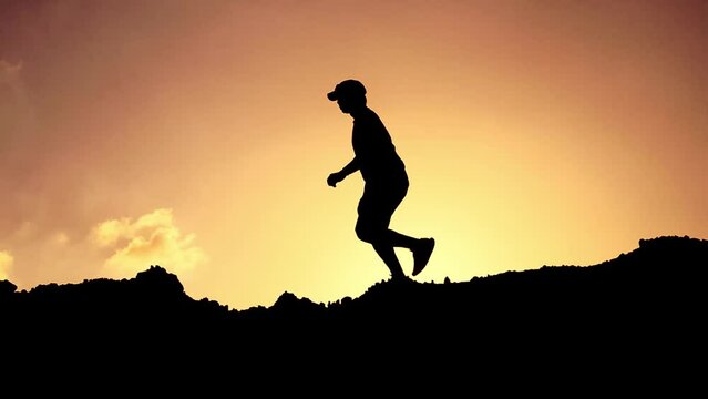 Silhouette of a happy and free man running a trail and exercising in the mountains.