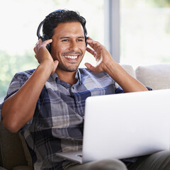 Man, laptop and living room with headphones, smile and internet for relax and streaming. Indian person, web and tech with house, lounge or apartment for listen to music or podcast with subscription