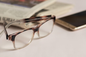 glasses newspaper smartphone on a light-colored background