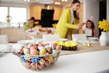 Easter eggs in basket on table at home with mother and daughter in background