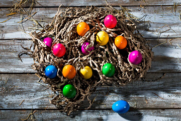 Easter nest of brown paper stripes with coloured Easter eggs on wood