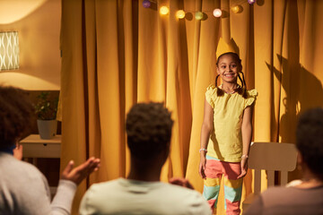 Portrait of smiling Black little girl standing on stage in makeshift theater and wearing princess...