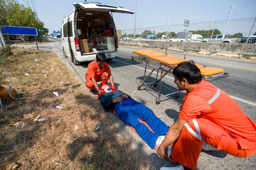 Two paramedic or emergency medical technician (EMT) in orange uniform helping neck and head...