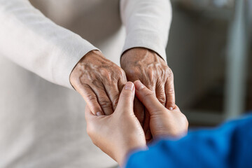 A female nurse caregiver holds hands to encourage and comfort an elderly woman. For care and trust...