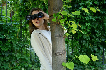Close-up of a young woman watching someone with binoculars while hiding