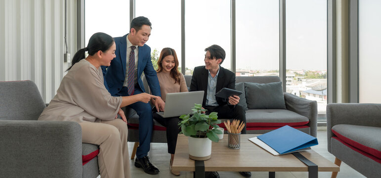 A group of business professional gathered around a small table in a modern office setting with large window that let in natural light. Young woman engaged in a discussion or presentation in a meeting.