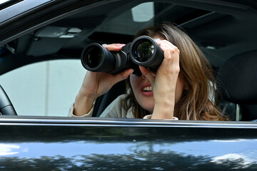 A young woman funny spying on someone through binoculars from a car