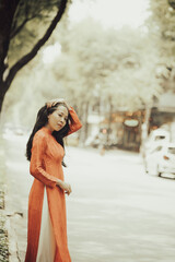 Naklejka premium Woman wearing traditional Vietnamese ao dai walking on the road of flying tamarind leaves.Portrait of woman wearing black sunglasses while standing behind friend.
