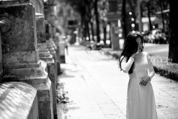 Woman wearing traditional Vietnamese ao dai walking on the road of flying tamarind leaves.Portrait of woman wearing black sunglasses while standing behind friend.