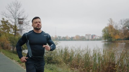 Attractive Man, Guy Jogging in the Park on a Background of Trees. Caucasian Runner Running. Morning Jog Sports Athletic Man in Black Sportswear. Jogging near the Local Lake. Healthy Lifestyle